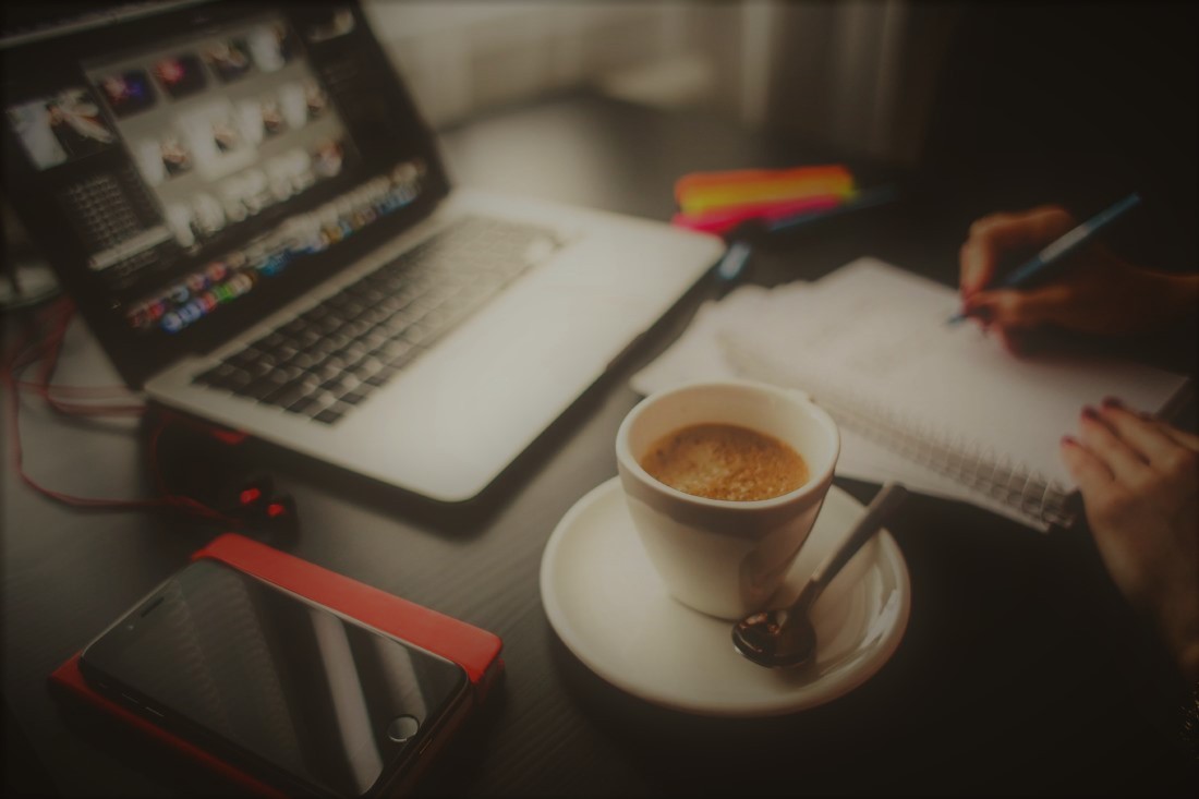 Foto de una persona trabajando con un ordenador portátil, una libreta, y un café