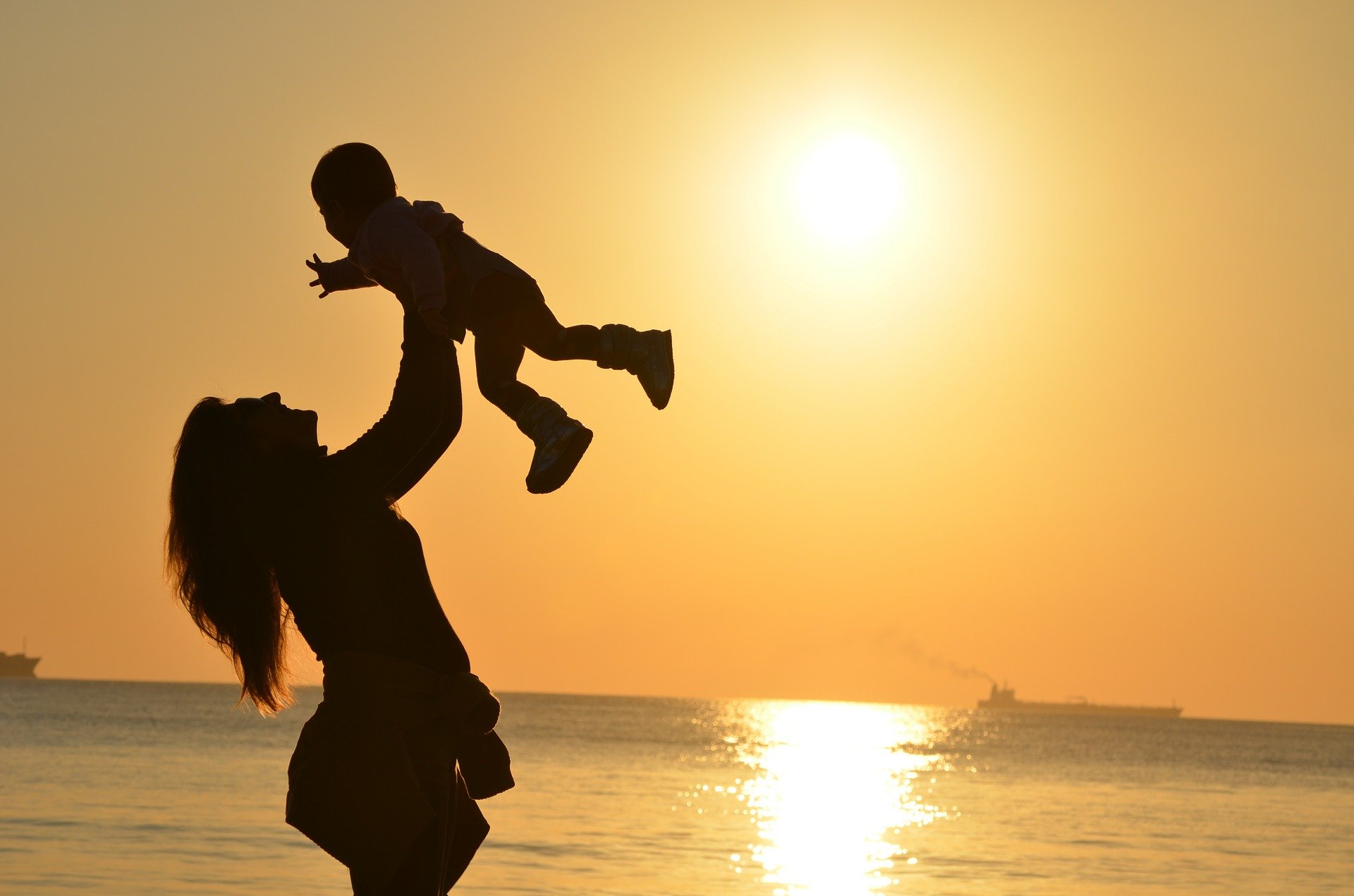 Foto de una mujer levantando a un niño con el sol de fondo