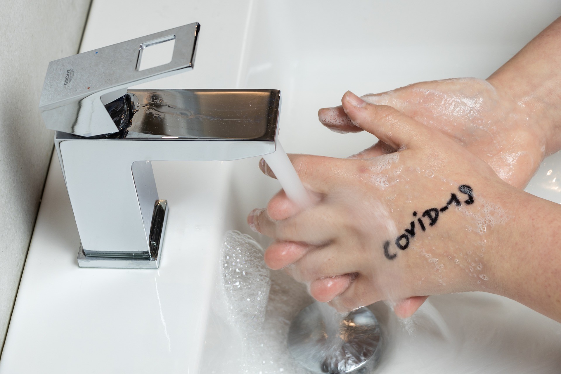 Foto de una persona lavándose la manos en las cuales dice "Covid-19"